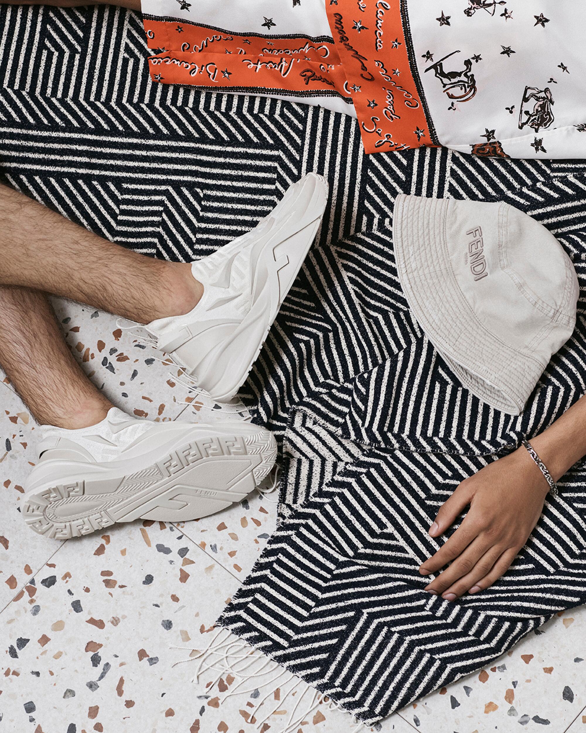 Feet in white sneakers rest next to a black-and-white striped outfit and a white bucket hat