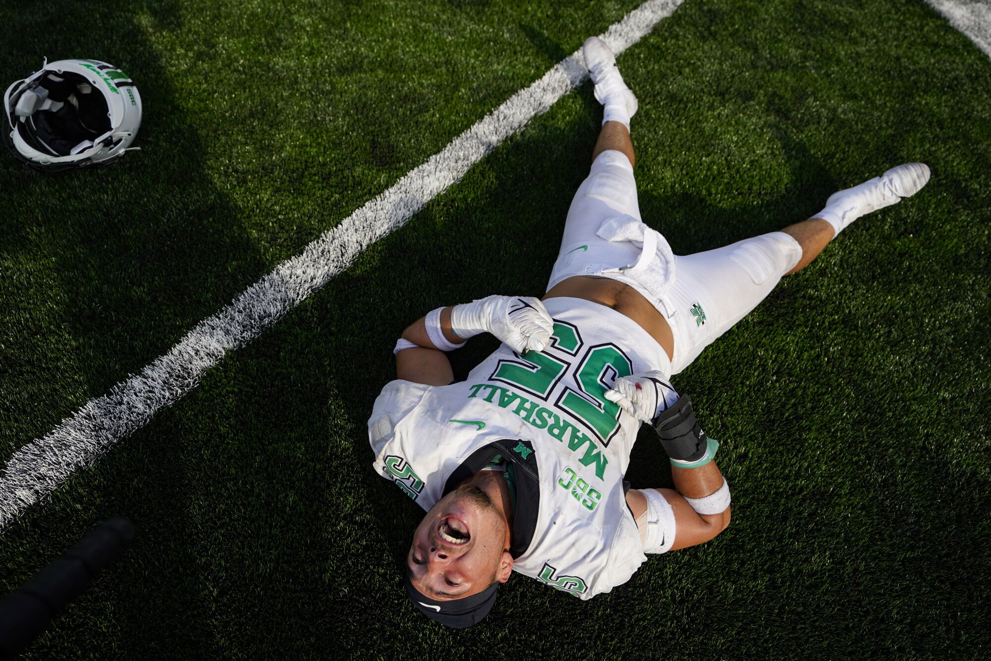 Marshall defensive lineman Owen Porter celebrates as he lays down on a green field.