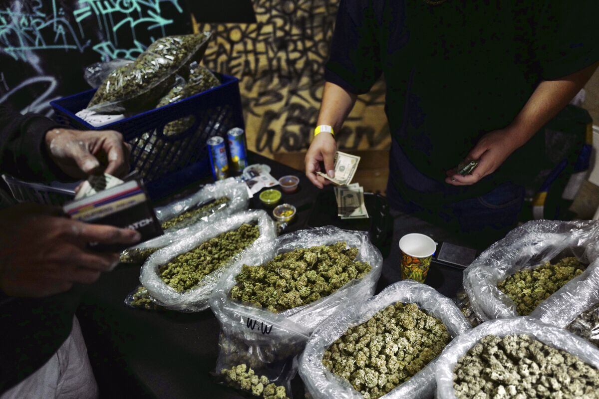 FILE - In this April 15, 2019, file photo, a vendor makes change for a marijuana customer at a cannabis marketplace in Los Angeles. An unwelcome trend is emerging in California, as the nation's most populous state enters its fifth year of broad legal marijuana sales. Industry experts say a growing number of license holders are secretly operating in the illegal market — working both sides of the economy to make ends meet. (AP Photo/Richard Vogel, File)