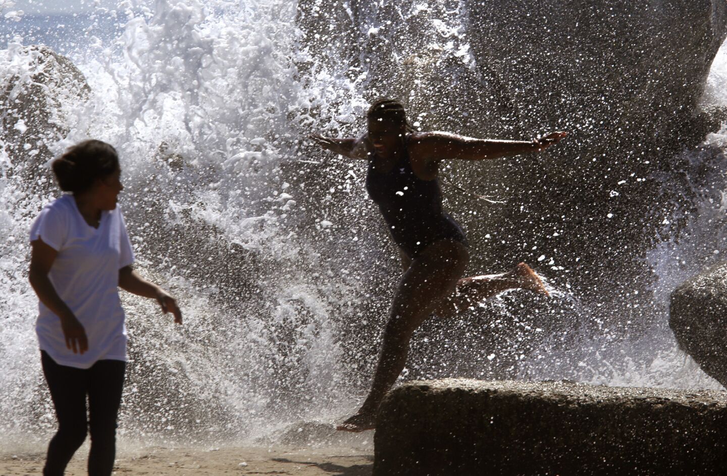 As temperatures soar into the 90s Thursday, Chevette Veney, 21, center, jumps through a splash over the breakwater at Venice Beach.