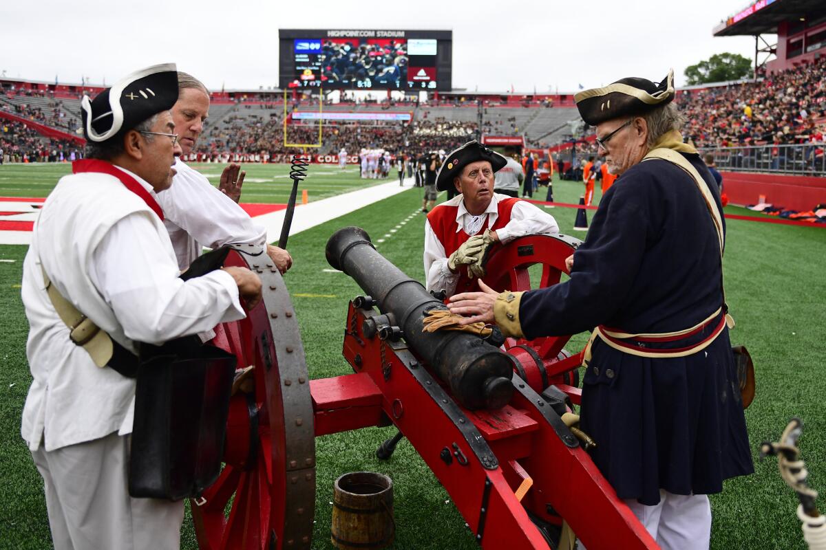 Men in Revolutionary War-era outfits stand next to a cannon on the sideline at a Rutgers football game.