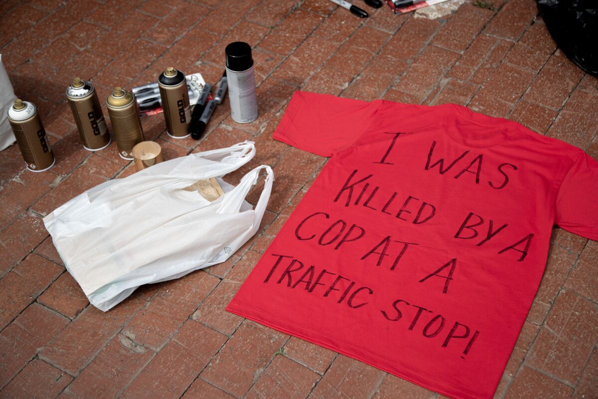 A red T-shirt lays on a ground with "I was killed by a cop at a traffic stop" text written on it.