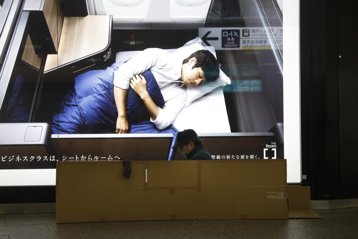 A homeless man sits in a cardboard box