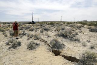 FILE - In this July 7, 2019 file photo, a visitor takes a photo of a crack in the ground following recent earthquakes near Ridgecrest, Calif. Scientists say the earthquakes that hammered the Southern California desert near the town of Ridgecrest last summer involved ruptures on a web of interconnected faults and increased strain on a major nearby fault that has begun to slowly move. (AP Photo/Marcio Jose Sanchez, File)
