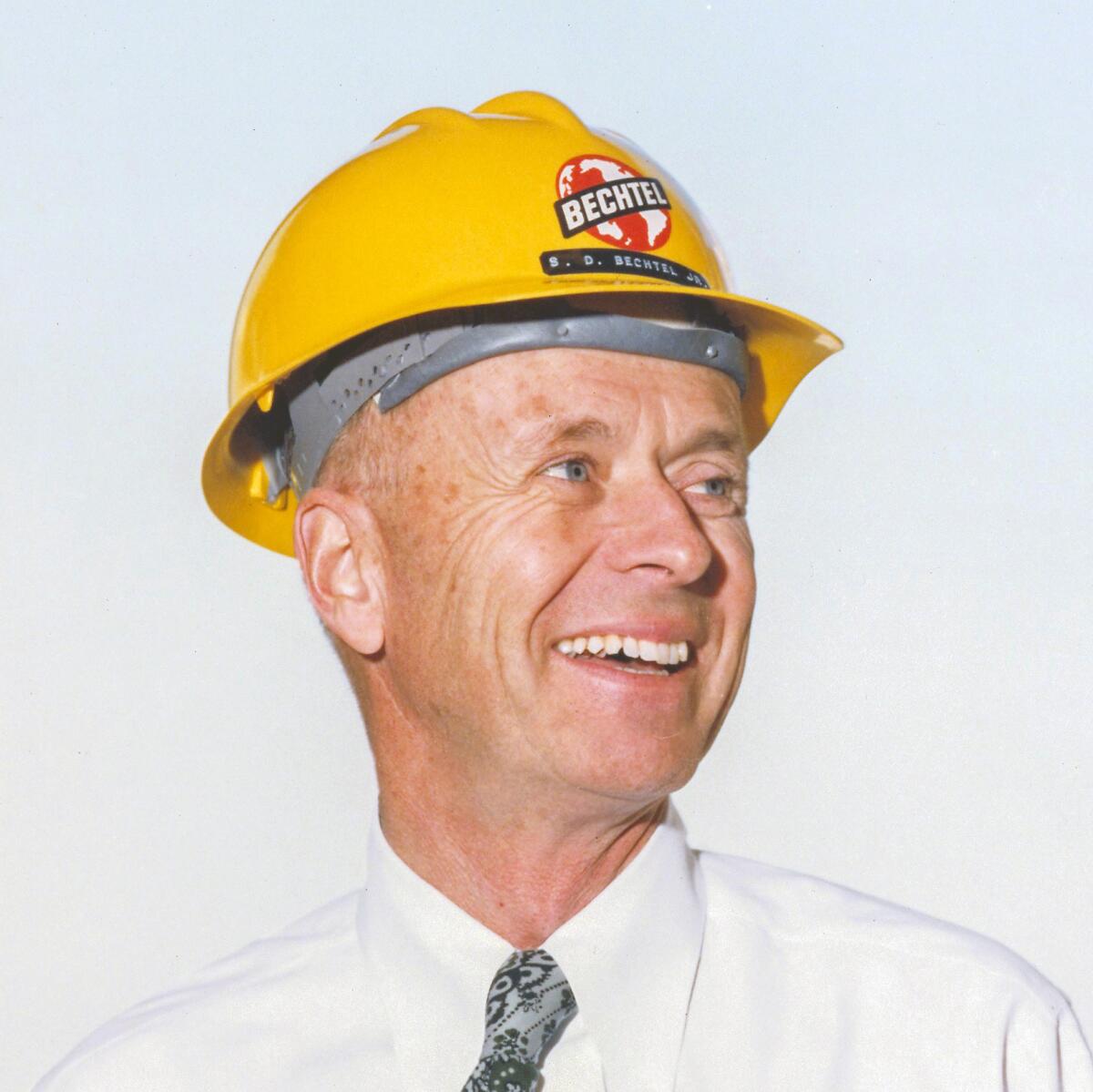Stephen Bechtel Jr. smiles while wearing a yellow hard hat in 1960.