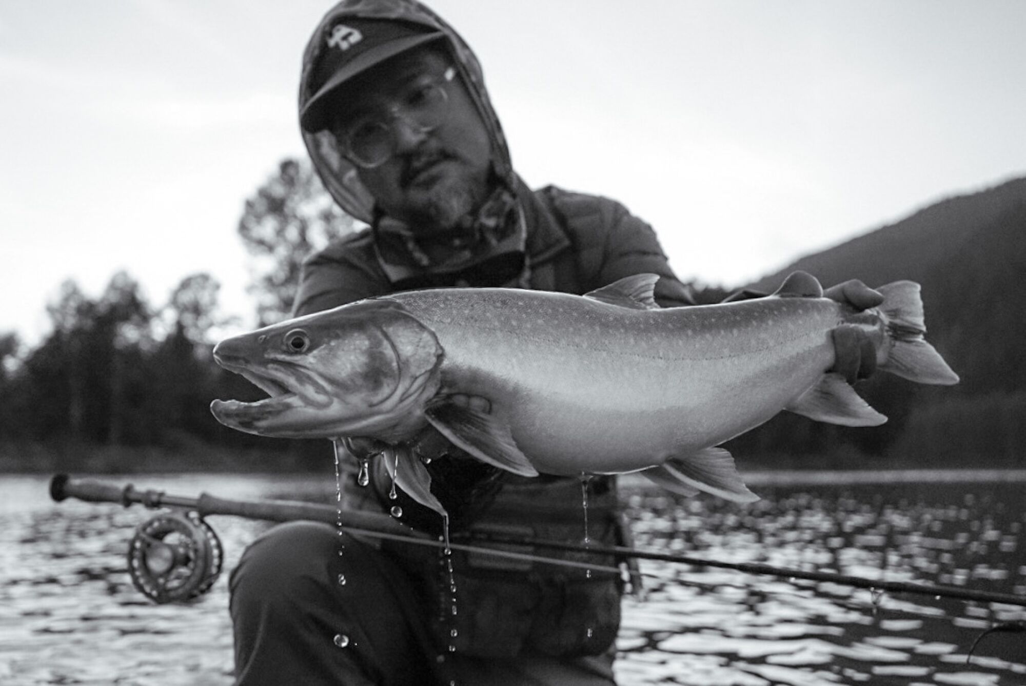 The artist holds up a fish, the river in the background