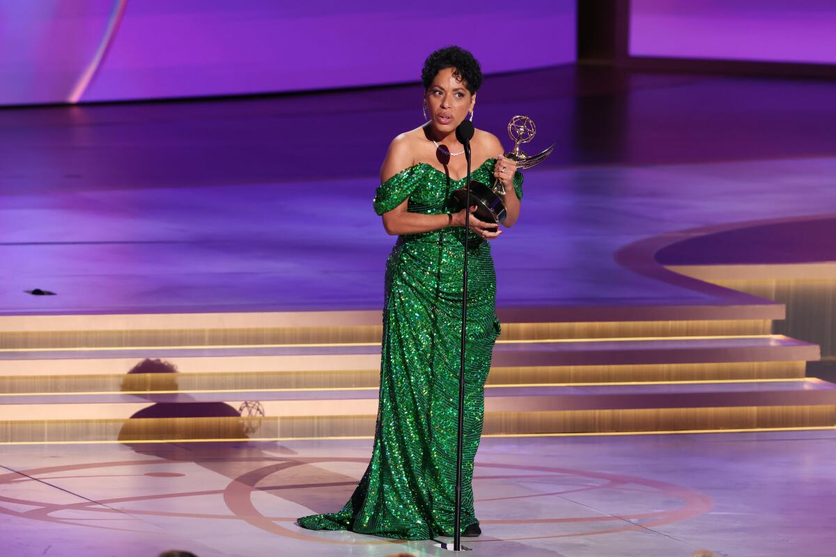 Liza Colon-Zayas, in a sequin green dress, holds an Emmy and delivers an acceptance speech on stage.