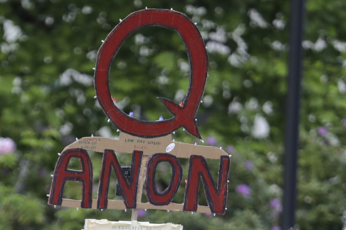 FILE - A person carries a sign supporting QAnon during a protest rally in Olympia, Wash., on May 14, 2020. The QAnon conspiracy theory has been linked to acts of real-world violence, including last year's riot at the U.S. Capitol. In June 2021, a federal intelligence report warned that QAnon adherents could target Democrats and other political opponents for more violence. (AP Photo/Ted S. Warren, File)