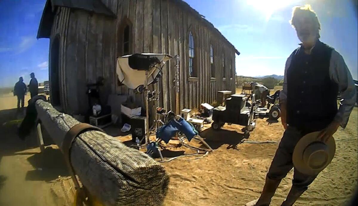 A fish-eye-lens photo of Alec Baldwin on the Western set of "Rust" next to a wood shack and a hitching post.