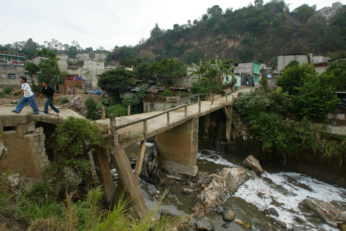 Slum dwellers cross a broken bridge spanning the muddy Rio Las Vacas in Guatemala City where Jose Antonio Guiterrez once lived with his alcoholic father, tubercular mother and two sisters. (Luis Sinco / Los Angeles Times)