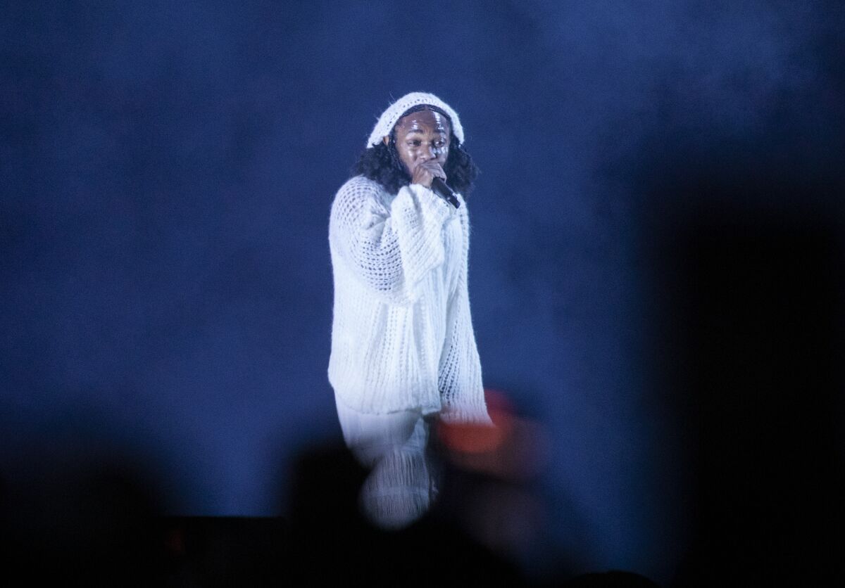 A man in a white beanie and sweater holding a microphone on a smokey stage