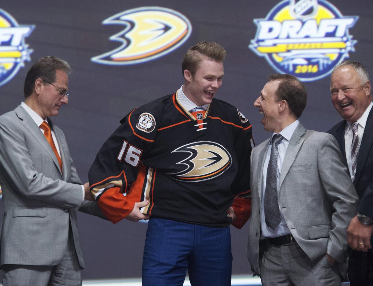 Max Jones smiles as he puts on his sweater while onstage with members of the Ducks management team after being drafted No. 24.