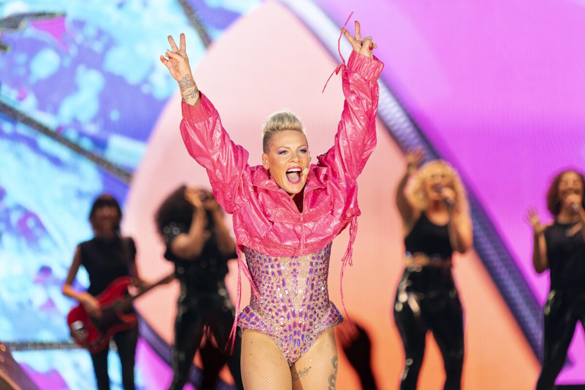 Pink raises her hands during a concert in a sparkly pink bodysuit and pink crop jacket in front of a backup singers