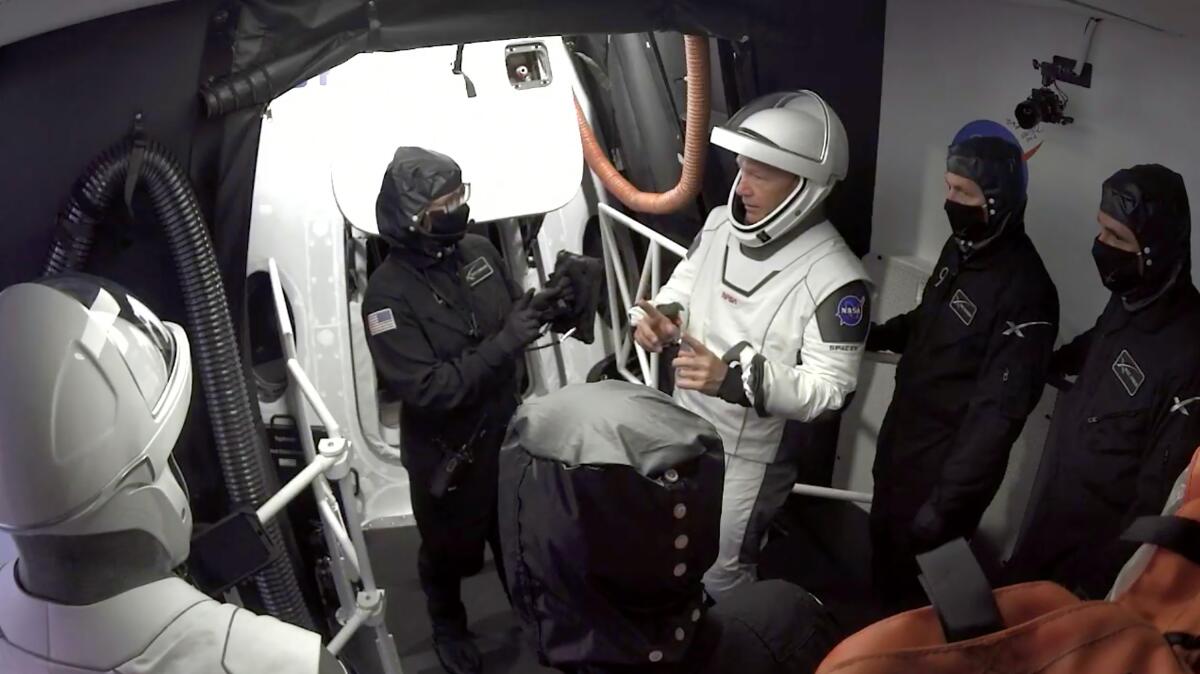In this Wednesday, May 27, 2020 image from video made available by SpaceX, NASA astronauts Doug Hurley, center, and Bob Behnken, left, confer with technicians after leaving the Crew Dragon capsule.
