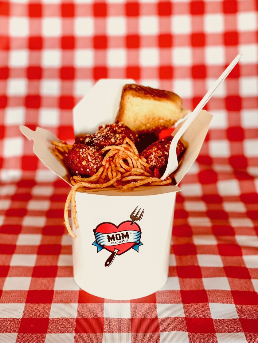 Spaghetti, meatballs and bread in a takeout container atop a checkered tablecloth.