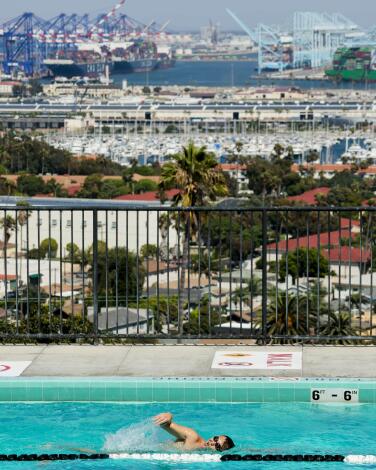 A man swims laps in a pool, with the harbor full of boats in the distance. 