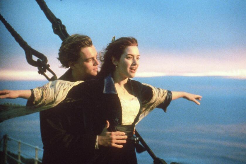Leonardo DiCaprio places a his hands on the waist of Kate Winslet, whose arms are outstretched at the front of a ship.