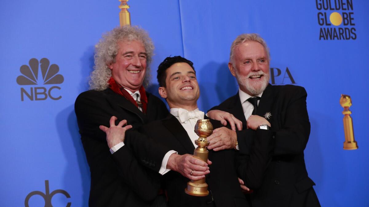 Rami Malek, center, stands with Queen members Brian May and Roger Taylor in the trophy room after winning his Golden Globe for "Bohemian Rhapsody."