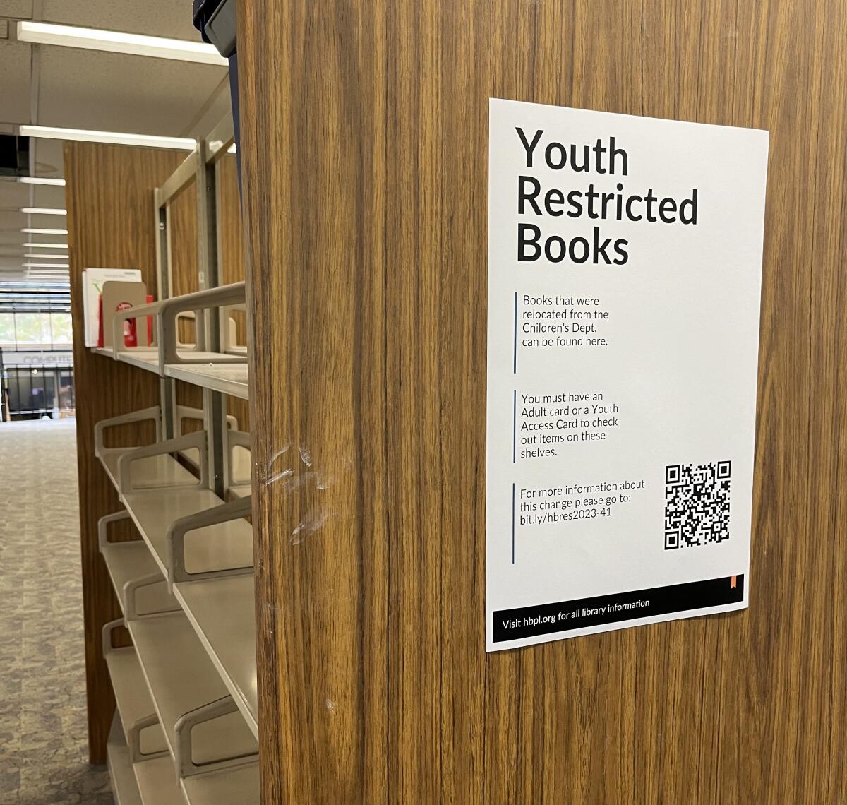 A mostly empty shelf of books with a sign reading "Youth restricted books"