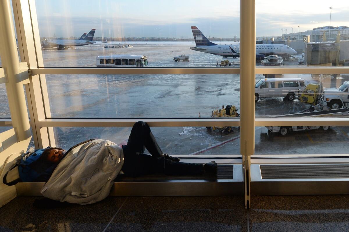 A man tries to sleep by a window at Ronald Reagan Washington National Airport in Arlington, Va. Airline delays and cancellations have cost passengers and carriers $5.8 billion this winter, a study has found.