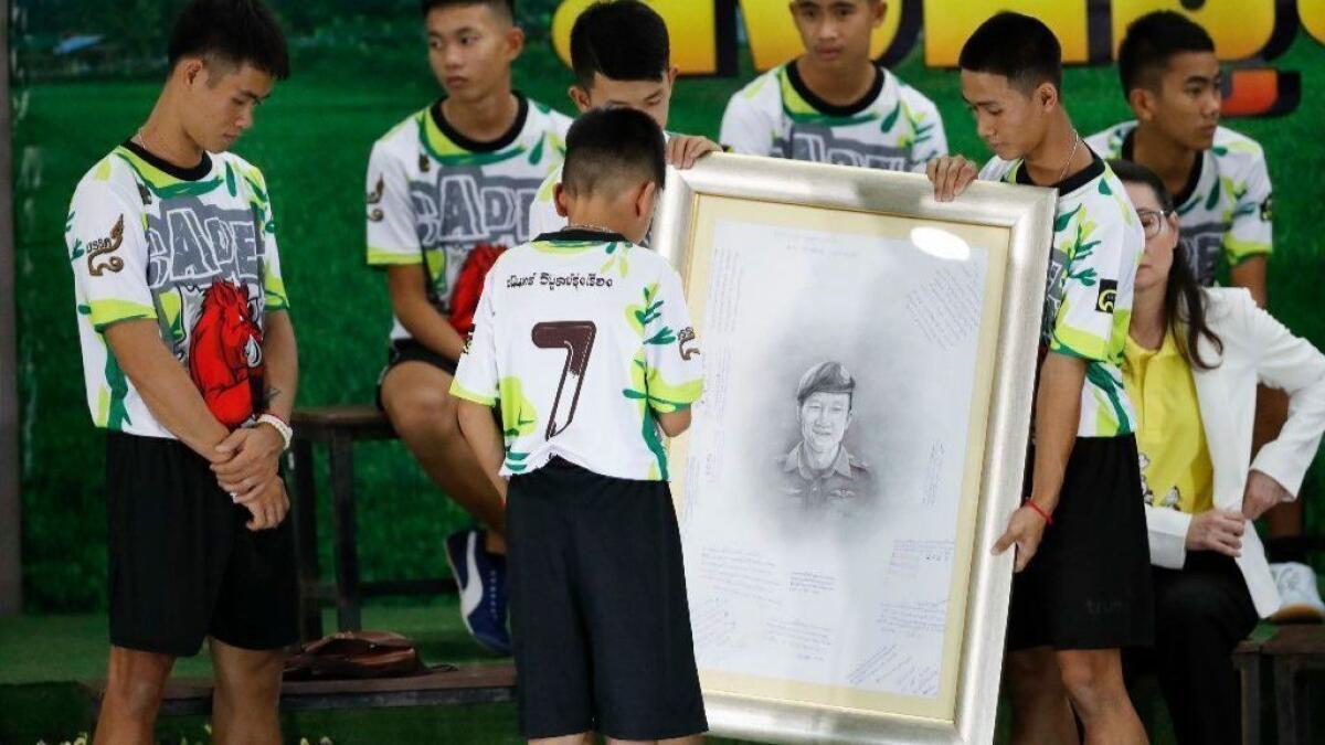 Coach Ekapol Chanthawong, left, and the 12 boys with a portrait of Saman Kunan, the retired Thai navy SEAL diver who died during the rescue operation.