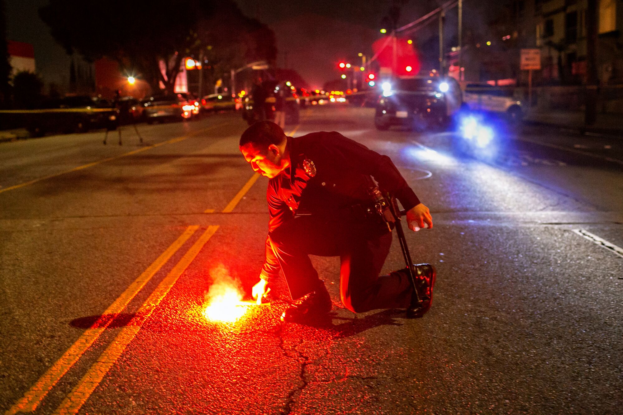 An LAPD officer launches a red flare in the middle of a road