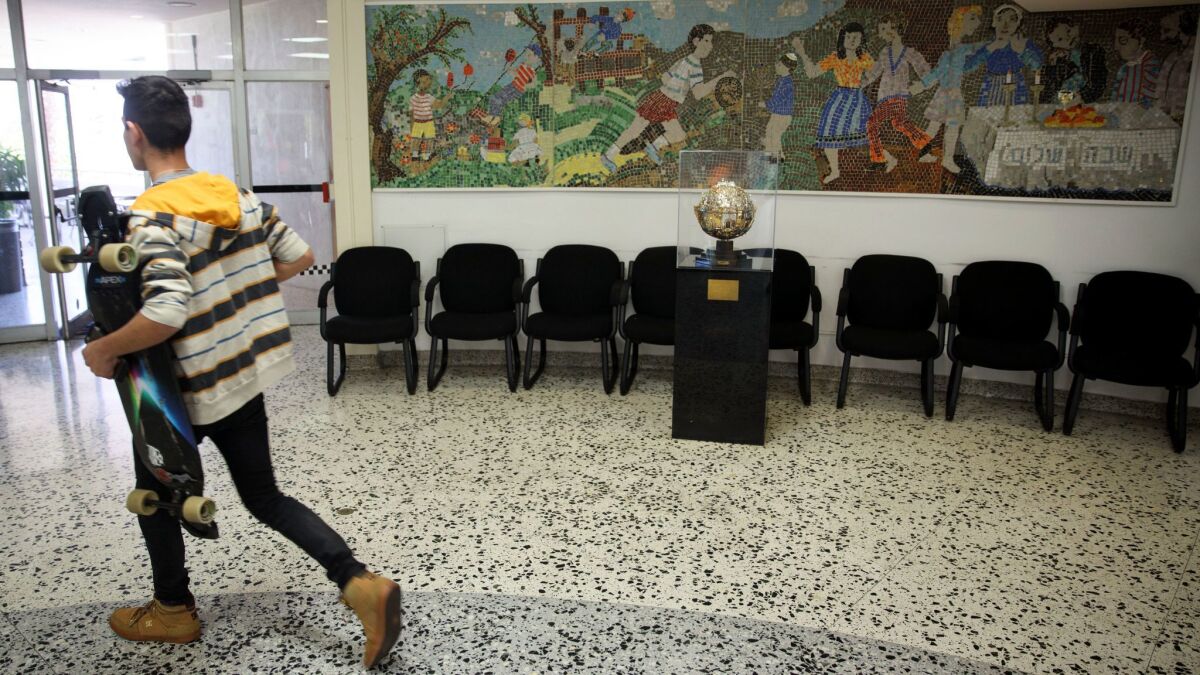A man carries a skateboard past a sculpture of the city of Jerusalem and a mural in the lobby of the Westside Jewish Community Center.