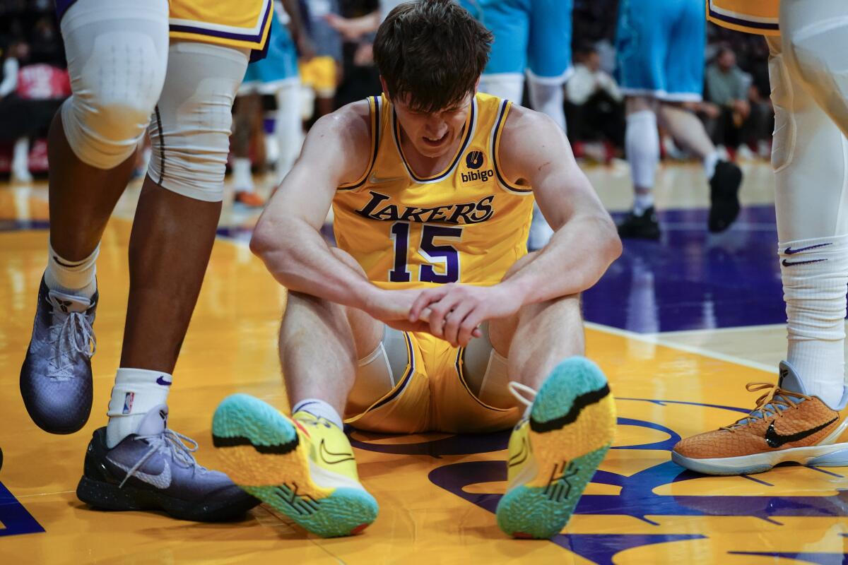 Lakers guard Austin Reaves sits on the court as teammates stand on either side