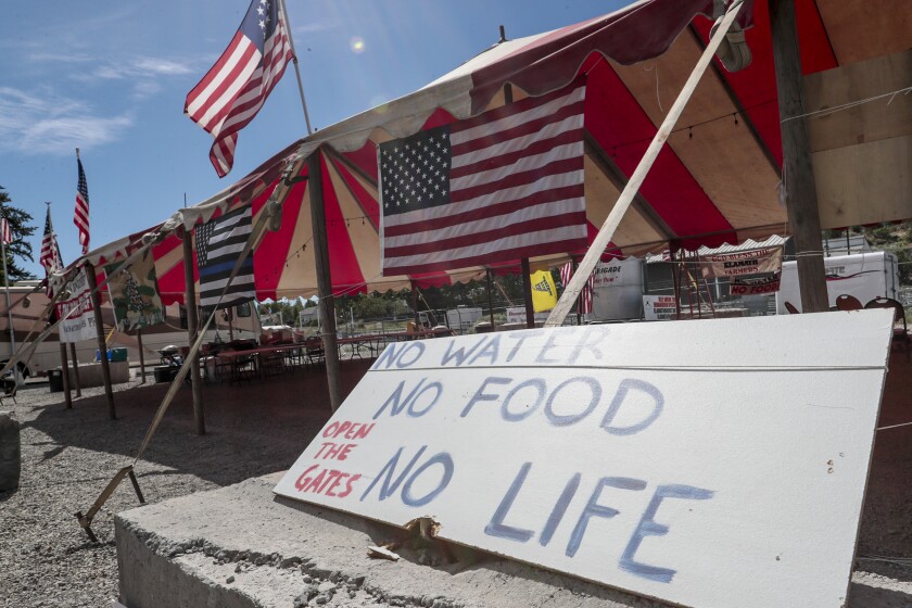 A circus tent decked with U.S. flags bears a sign saying, "Open the gates. No water, no food, no life."