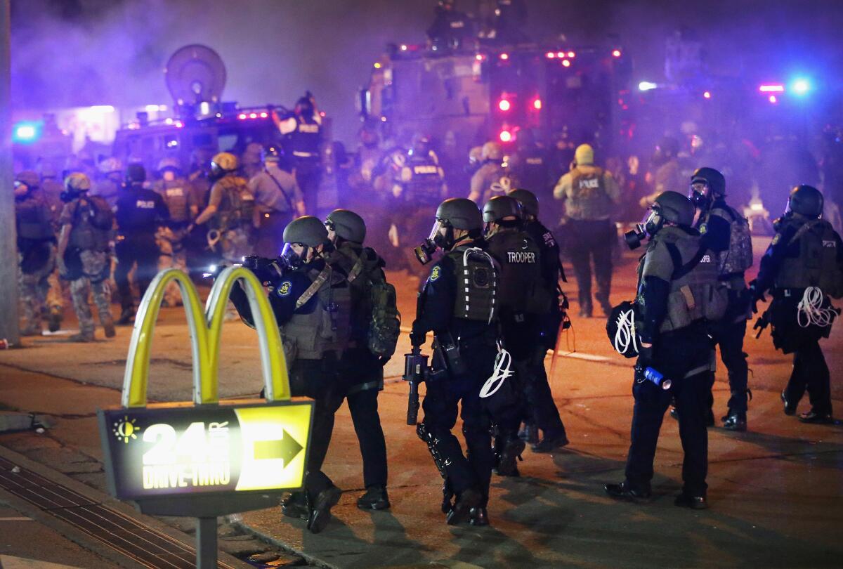 Officers in riot gear walk past a McDonald's drive-thru sign during protests in Ferguson, Mo.