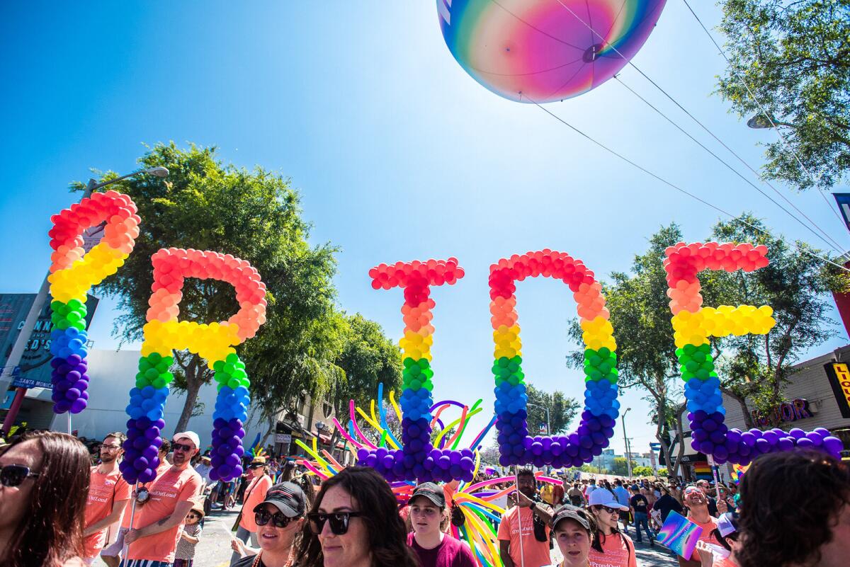 A group of people hold balloons in the air that spell the word Pride