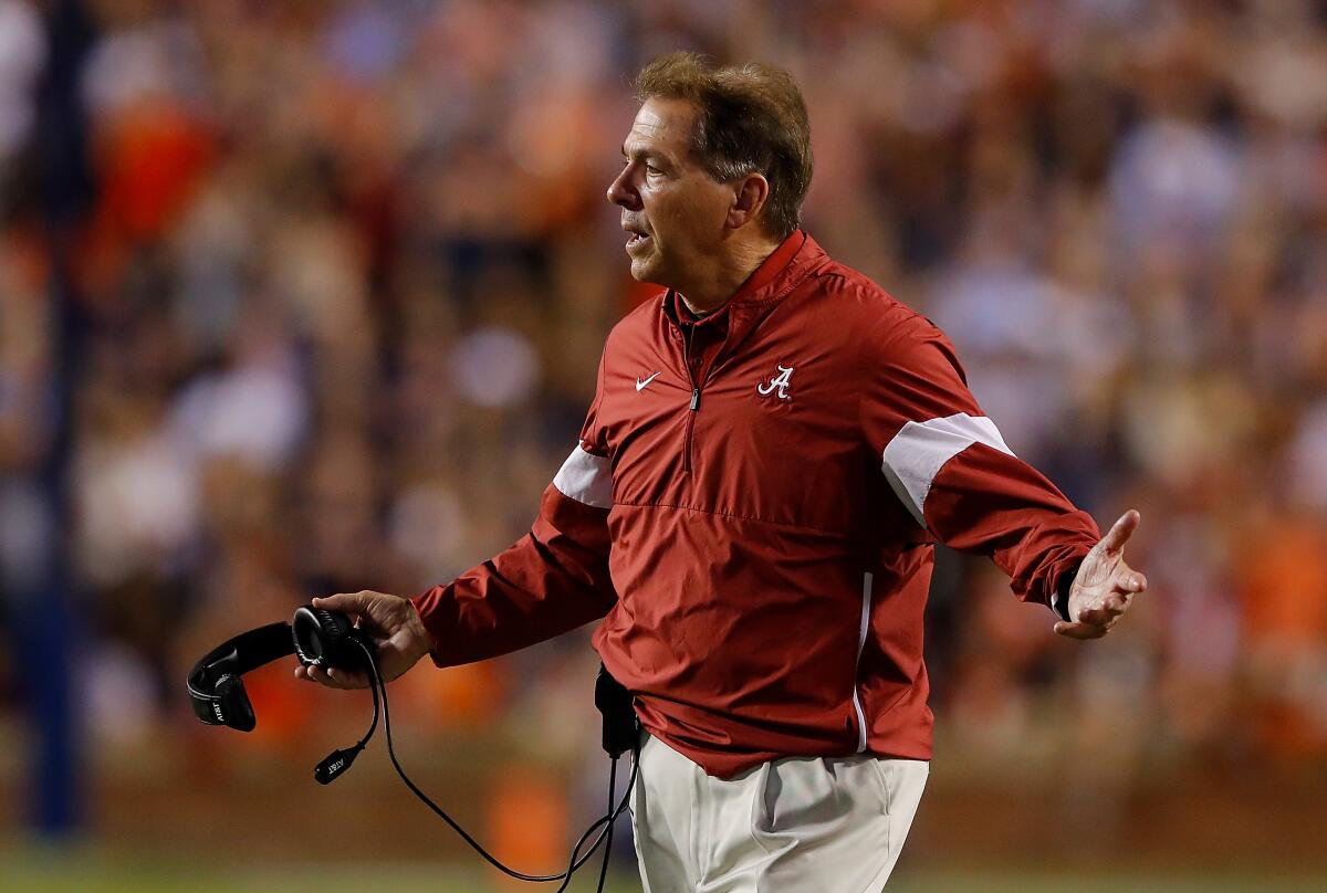 Coach Nick Saban holds out his arms at a football game