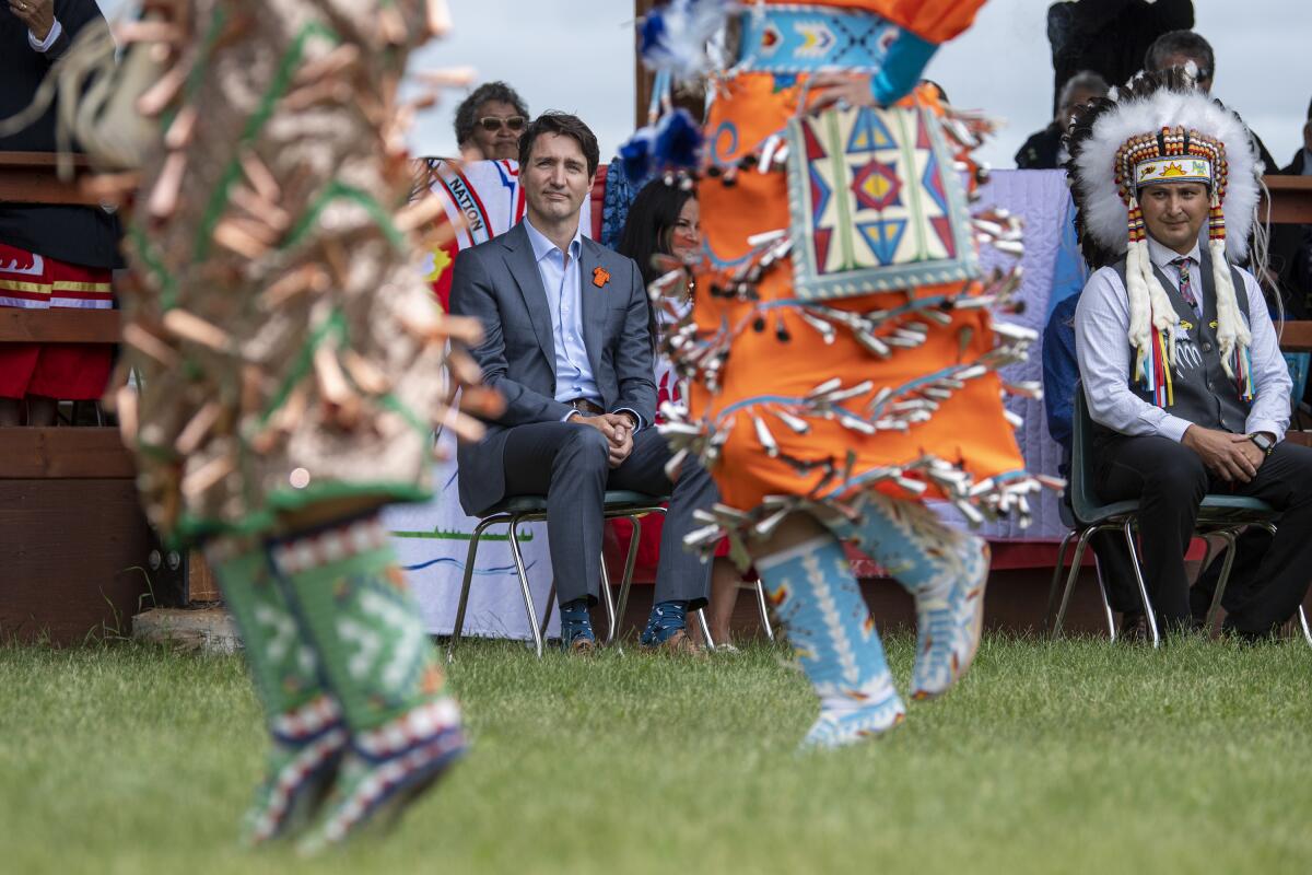 Prime Minister Justin Trudeau, left, and Chief Cadmus Delorme watch dancers during a ceremony celebrating the signing of a transfer of control over children in care to the community, in Cowessess First Nation, Saskatchewan, Tuesday, July 6, 2021. Cowessess is also the site of a former residential school where, the month before, ground-penetrating radar detected a potential 751 unmarked graves. (Liam Richards/The Canadian Press via AP)
