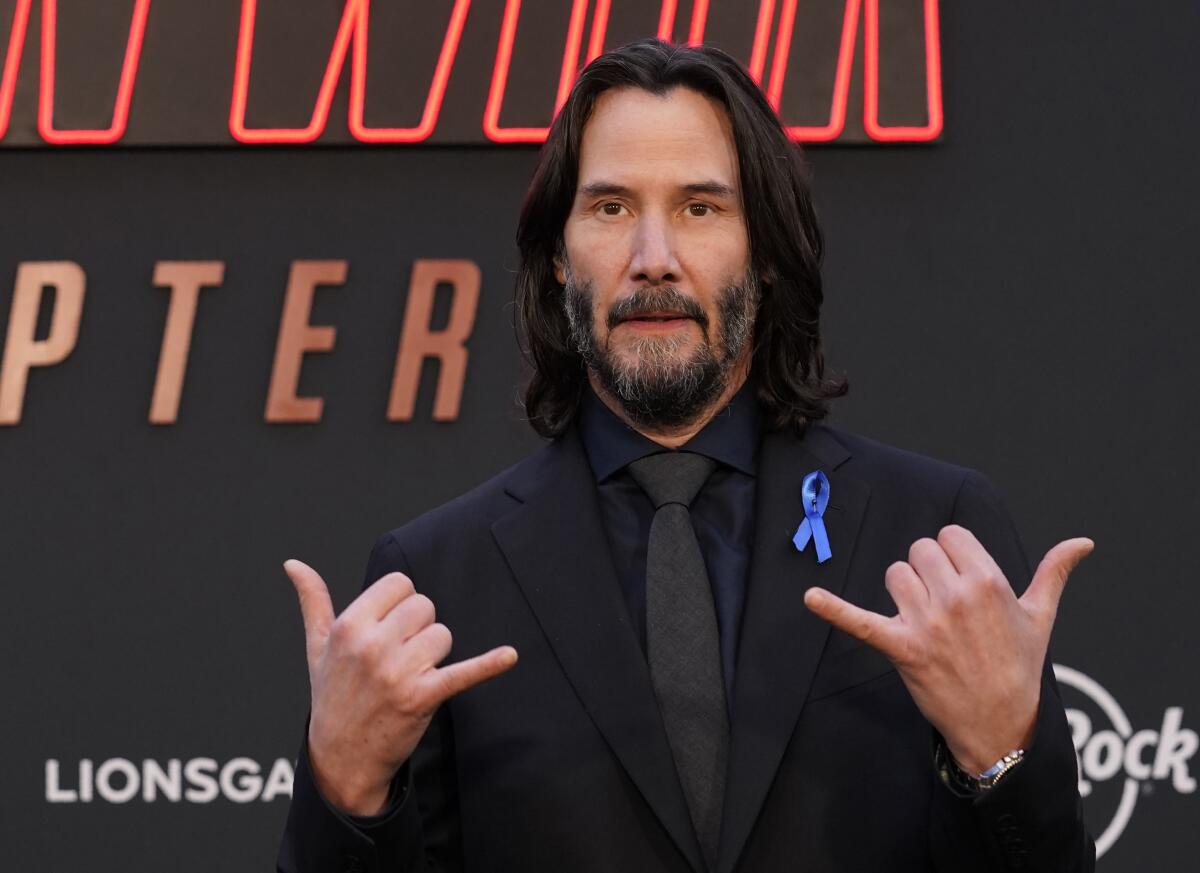 Keanu Reeves makes shaka signs with his hands at a movie premiere