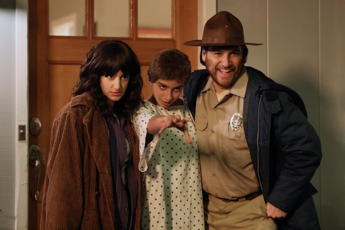 A woman, a child and a man in a sheriff's uniform pose for a photo in front of a door.