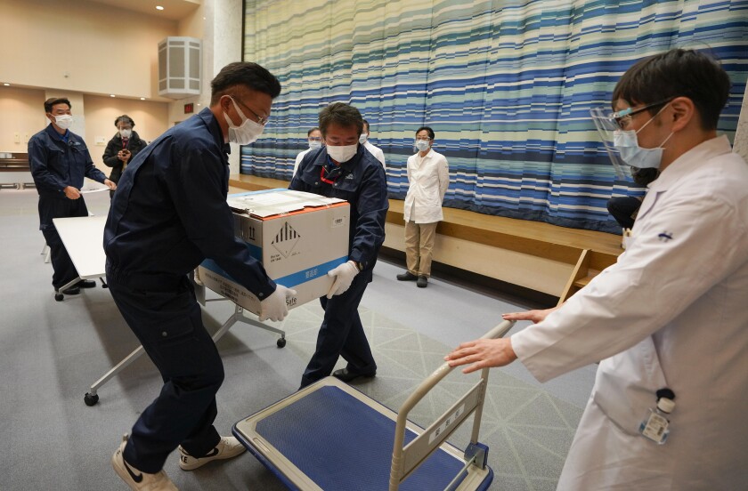 Delivery staff move a box of Pfizer Inc's COVID-19 vaccine on a carriage at the hospital in Tokyo, Japan, Tuesday, Feb. 16, 2021. Japan's COVID-19 vaccinations are scheduled to begin Wednesday after the government granted belated first approval to a shot co-developed by Pfizer Inc. (Kimimasa Mayama/Pool Photo via AP)