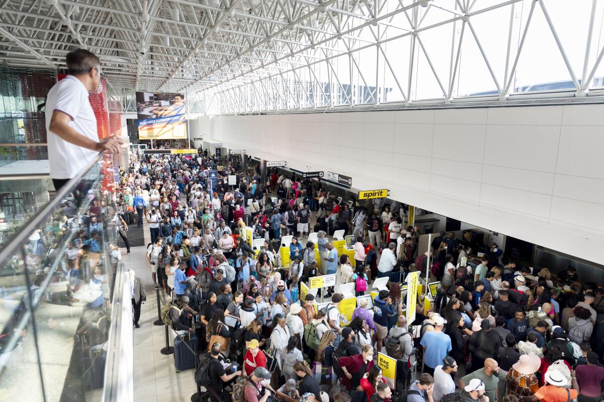People wait in lines at an airport as a person above them looks from a glass railing.