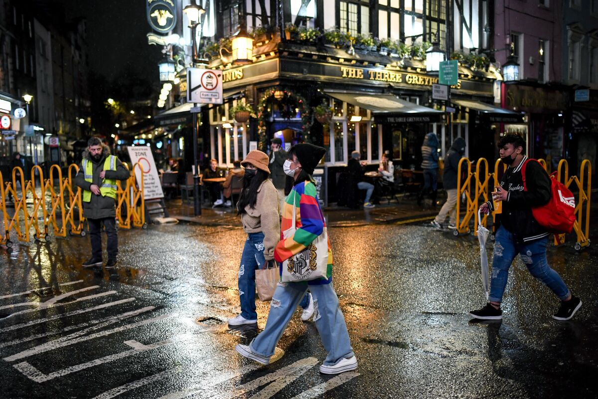People wearing face masks to protect against coronavirus as they walk past a pub in Soho, London, Monday, Dec. 14, 2020. London and its surrounding areas will be placed under Britain's highest level of coronavirus restrictions beginning Wednesday as infections rise rapidly in the capital, the health secretary said Monday, adding that a new variant of the virus may be to blame for the spread. (AP Photo/Alberto Pezzali)