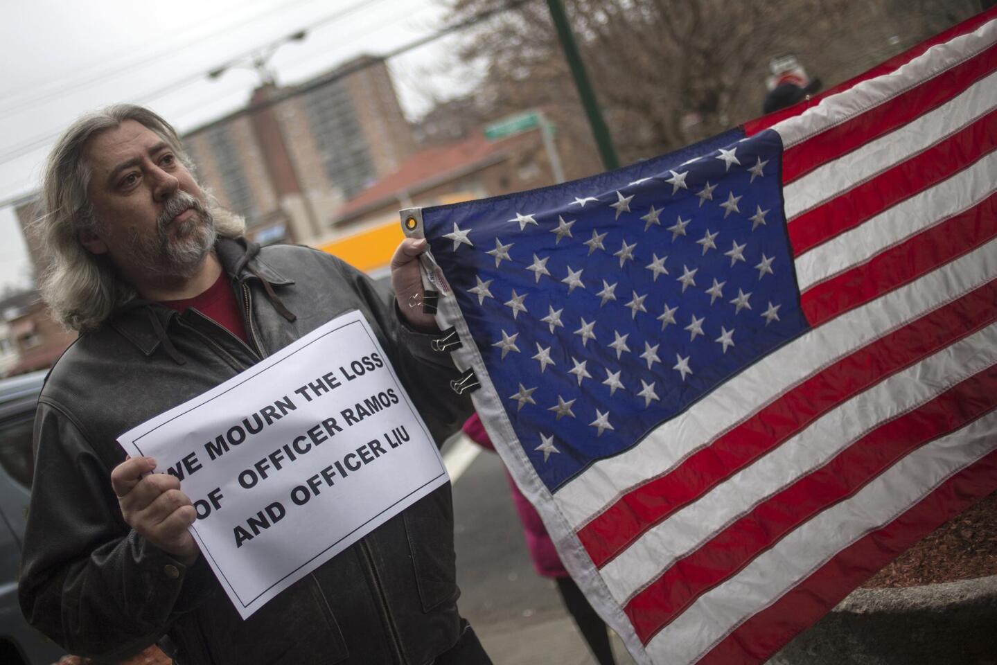 A man holds a sign and the American flag as he gathers with dozens to show support for policemen in New York