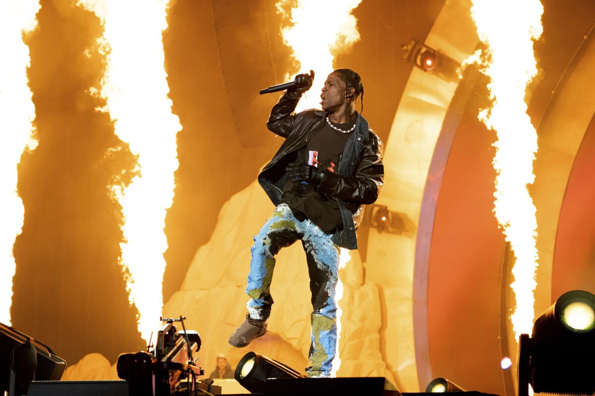Travis Scott holding a microphone and dancing onstage in front of pyrotechnics