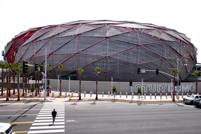 INGLEWOOD, CA - AUGUST 1, 2024 - A pedestrian cross Prairie Avenue against a backdrop of the Intuit Dome Plaza in Inglewood on August 1, 2024. The sports stadium is still under construction. (Genaro Molina/Los Angeles Times)