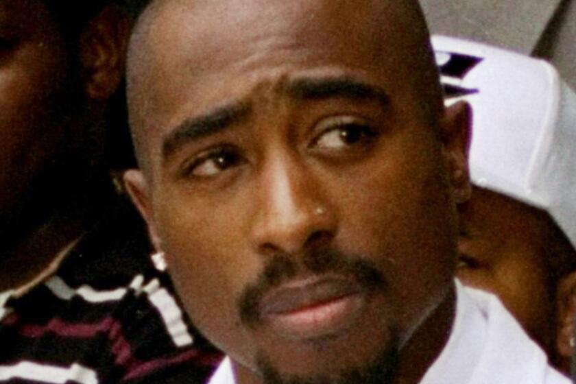 An old photo of Tupac Shakur wearing a white suit and looking to his left.