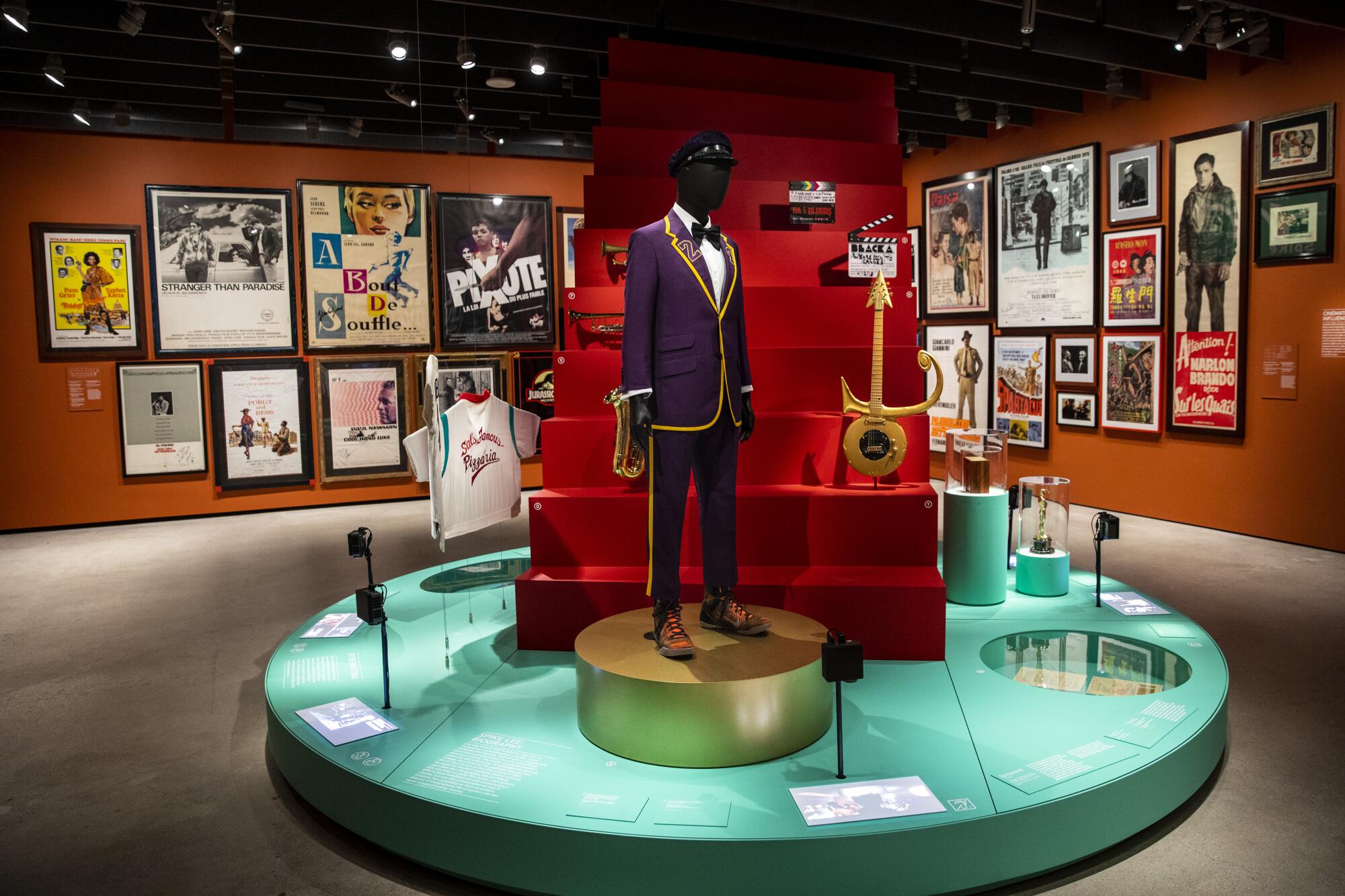 A platform houses a mannequin wearing a purple suit, a red staircase with a Prince guitar on it, a jersey and a statuette