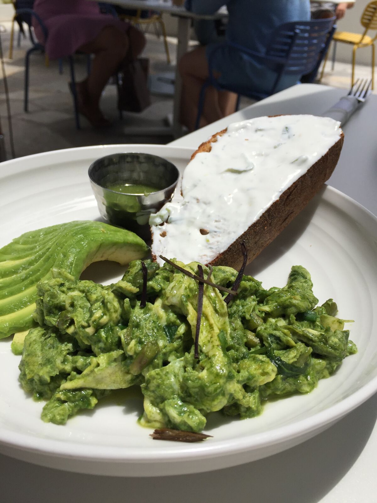 Organic green scrambled eggs at Parakeet Cafe. The dish includes kale, asparagus, green beans, avocado and salsa verde with a side of toast with labneh spread.
