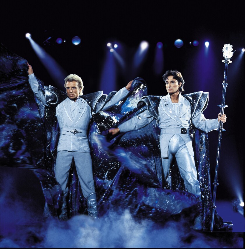 Two men in lavish capes perform onstage.