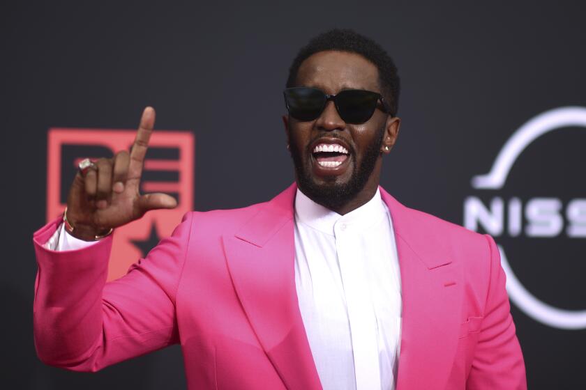 A man wearing a pink suit and sunglasses and holding up his pointer finger