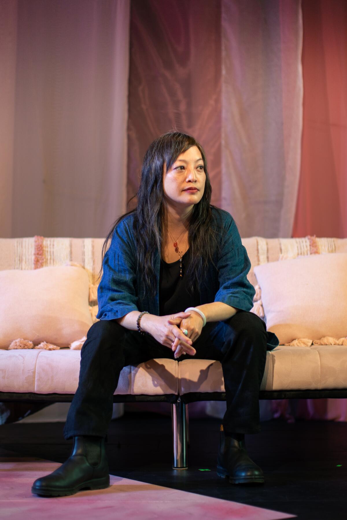 A woman sits on a couch onstage 