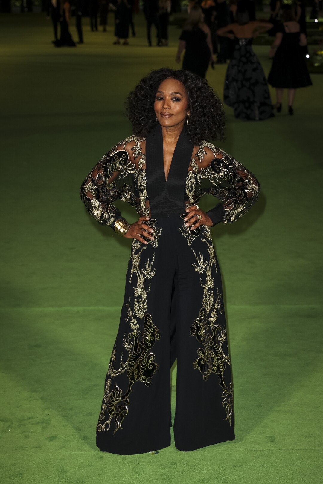 A woman in a patterned, black jumpsuit posing on a green carpet