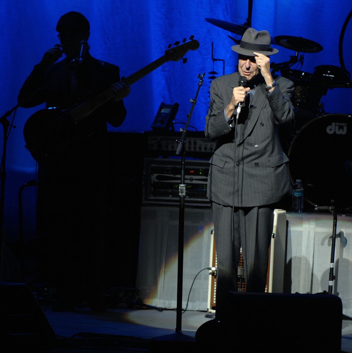 Leonard Cohen, right, performs onstage in a gray double-breasted suit and matching hat