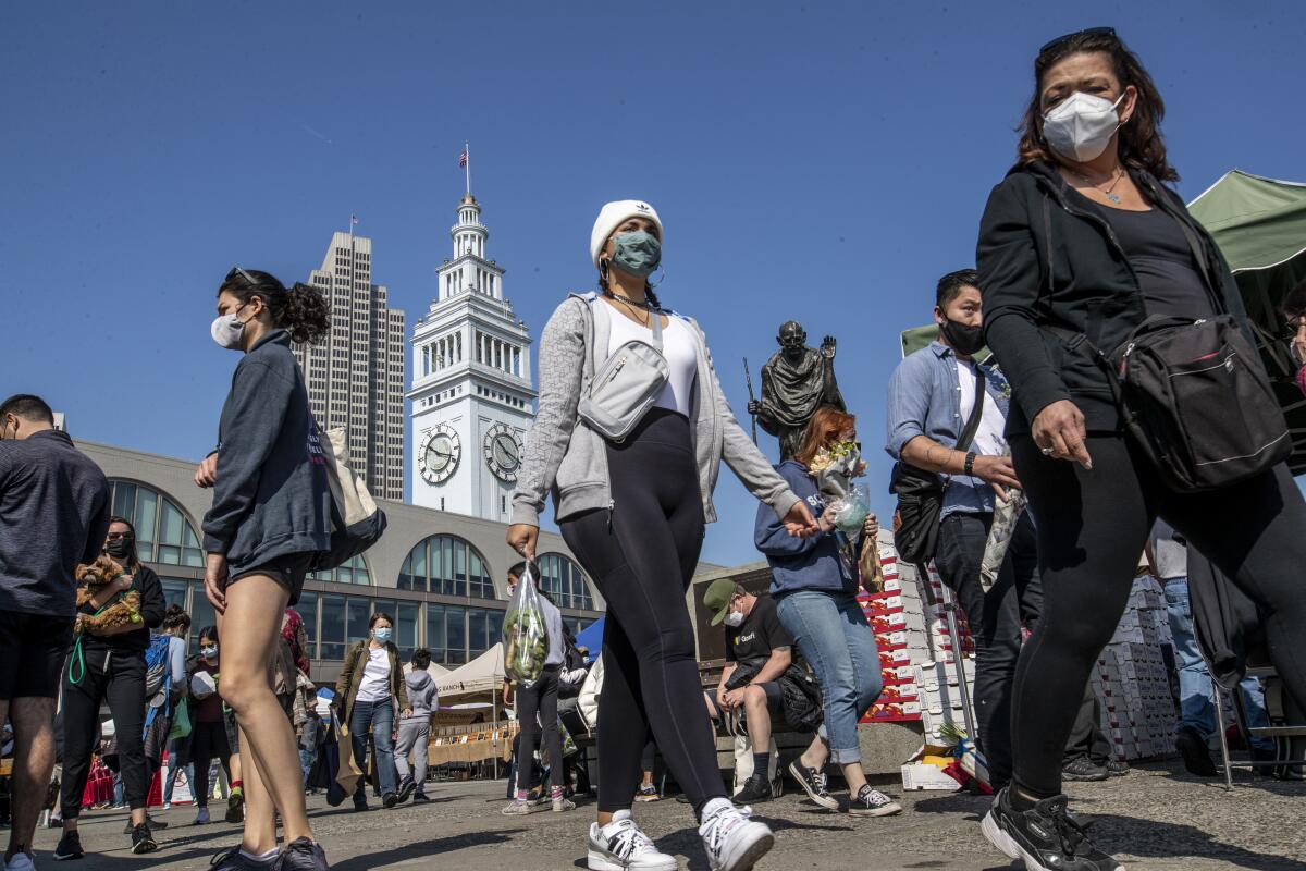 People in masks walk around the Embarcadero in San Francisco.